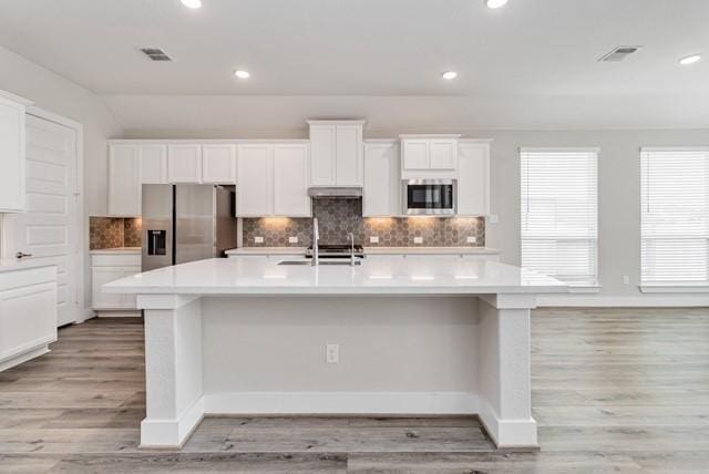 kitchen featuring appliances with stainless steel finishes, white cabinetry, a large island, decorative backsplash, and visible vents