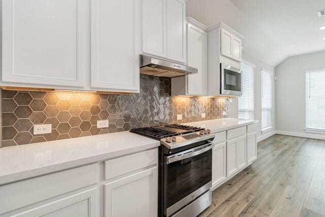 kitchen with light countertops, under cabinet range hood, white cabinets, appliances with stainless steel finishes, and vaulted ceiling