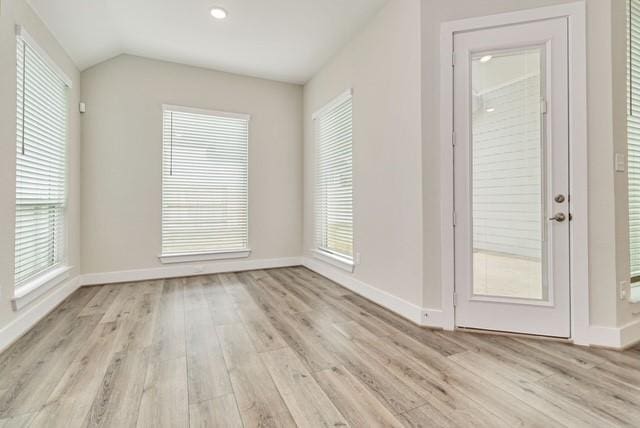 spare room with baseboards, vaulted ceiling, and light wood-type flooring
