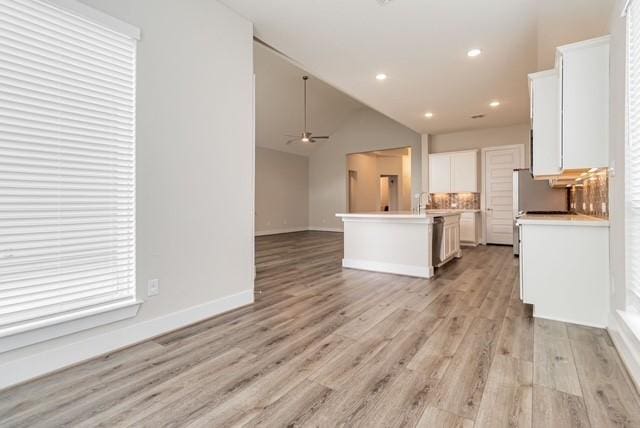 kitchen with light countertops, baseboards, white cabinets, open floor plan, and light wood-style flooring