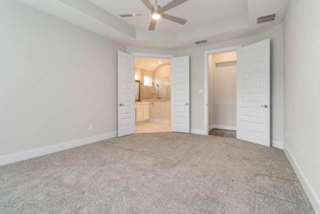 unfurnished bedroom with visible vents, a raised ceiling, carpet, and ensuite bath