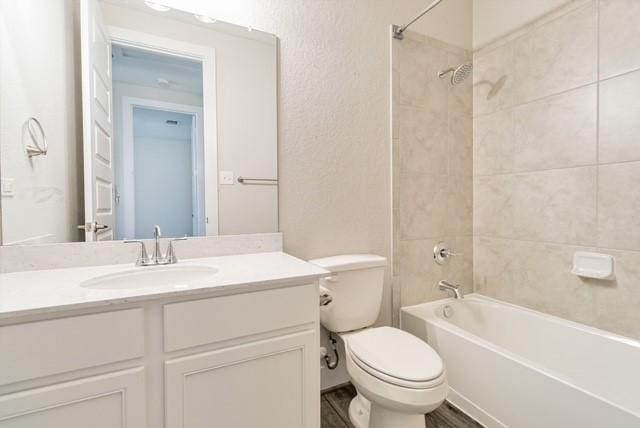 full bathroom with toilet,  shower combination, a textured wall, and vanity