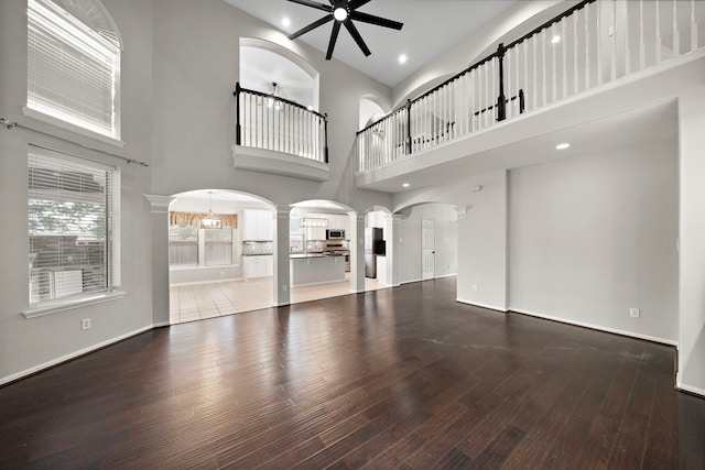 3615 Caleb Ln, Missouri City, TX 77459 - unfurnished living room featuring decorative columns, wood-type flooring, arched walkways, a ceiling fan, and a towering ceiling