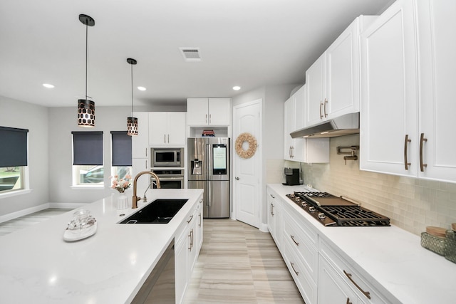 kitchen featuring appliances with stainless steel finishes, a sink, under cabinet range hood, backsplash, and white cabinetry