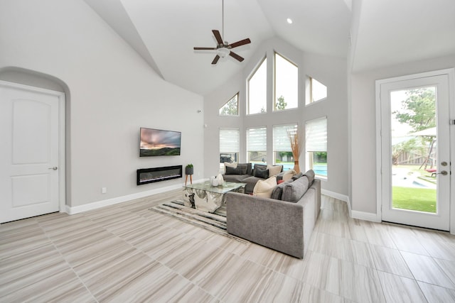 living room featuring high vaulted ceiling, ceiling fan, plenty of natural light, a glass covered fireplace, and baseboards