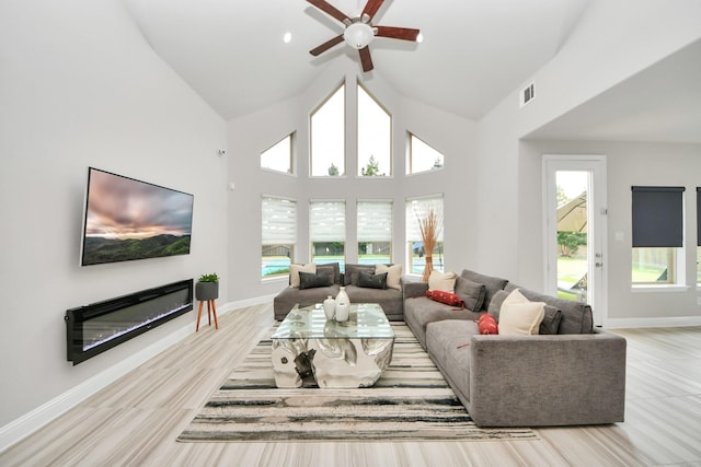 living area featuring a glass covered fireplace, ceiling fan, baseboards, and high vaulted ceiling
