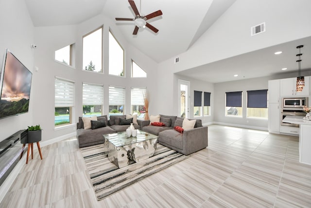 living area with a ceiling fan, plenty of natural light, high vaulted ceiling, light tile patterned flooring, and baseboards