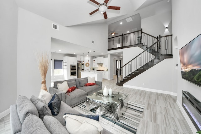 living room featuring a ceiling fan, stairway, a towering ceiling, baseboards, and recessed lighting