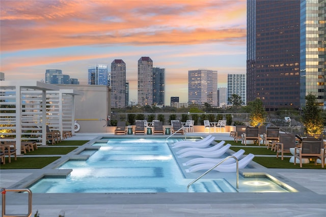 pool at dusk featuring a community pool, a view of city, fence, and a patio