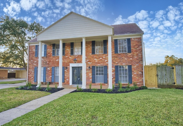 greek revival inspired property featuring fence, brick siding, a front yard, a gate, and french doors