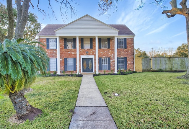 neoclassical home with fence, brick siding, and a front yard