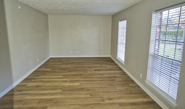 empty room with baseboards, a textured ceiling, a textured wall, and wood finished floors