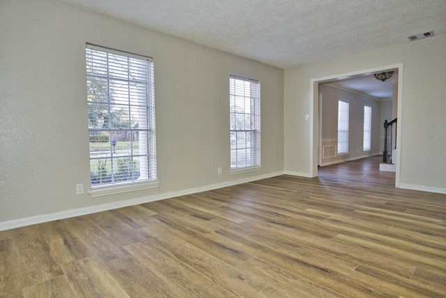 unfurnished room featuring baseboards, a textured ceiling, wood finished floors, and visible vents