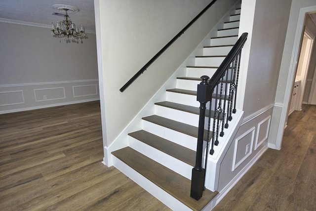 staircase with crown molding, visible vents, wood finished floors, a decorative wall, and a chandelier
