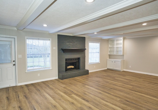 unfurnished living room with a fireplace, a textured ceiling, plenty of natural light, wood finished floors, and beamed ceiling