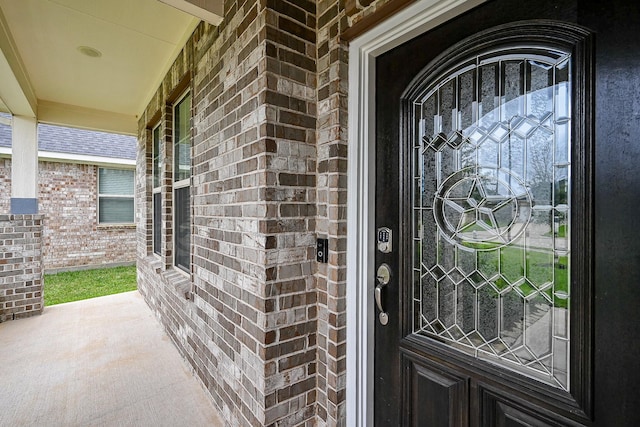 view of exterior entry with a porch and brick siding
