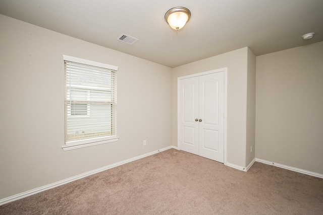 unfurnished bedroom with baseboards, visible vents, a closet, and light colored carpet