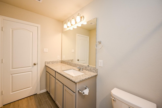 bathroom with visible vents, wood finished floors, vanity, baseboards, and toilet