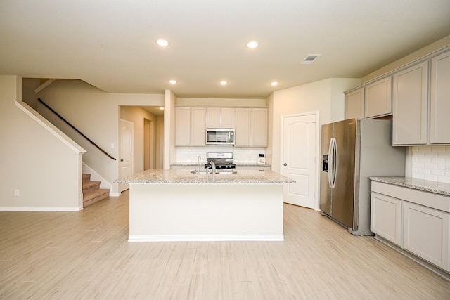kitchen featuring visible vents, a center island with sink, tasteful backsplash, and stainless steel appliances