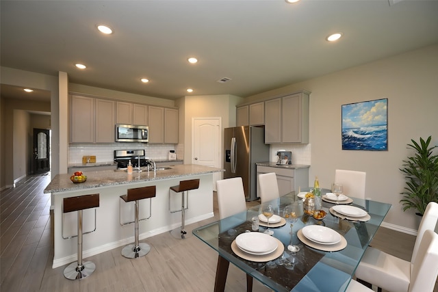 kitchen featuring gray cabinets, backsplash, a kitchen bar, and stainless steel appliances