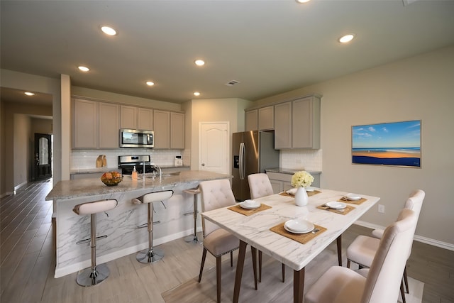 kitchen featuring appliances with stainless steel finishes, gray cabinets, a breakfast bar area, and backsplash