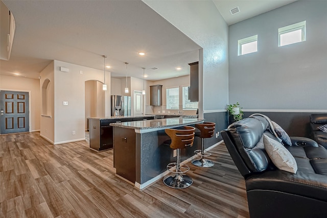 kitchen with wood finished floors, a breakfast bar, open floor plan, stainless steel refrigerator with ice dispenser, and arched walkways