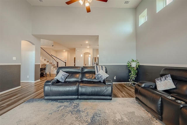 living room featuring ceiling fan, arched walkways, wood finished floors, stairway, and a high ceiling