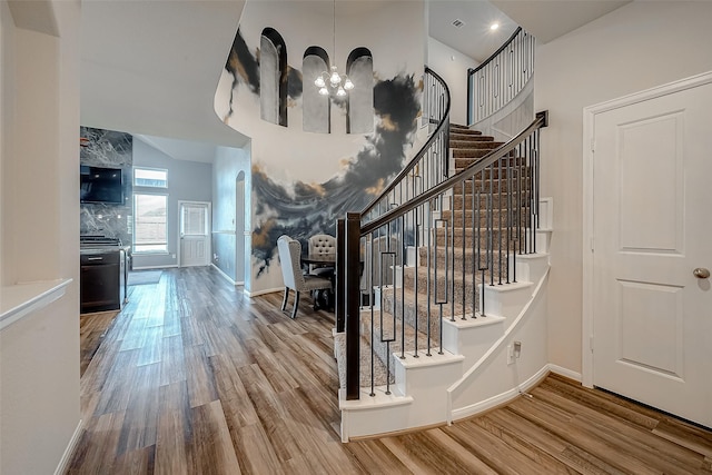 staircase with an inviting chandelier, baseboards, wood finished floors, and a towering ceiling