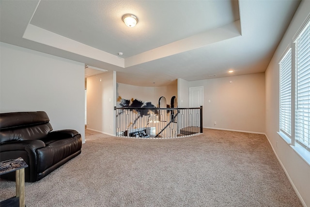 living area featuring carpet floors, a tray ceiling, an upstairs landing, and attic access