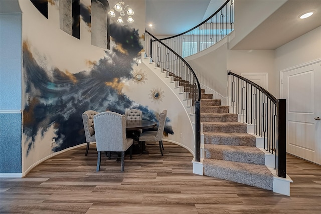 stairway featuring baseboards, a high ceiling, and wood finished floors
