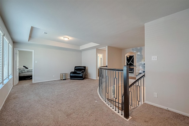 corridor with carpet floors, baseboards, an upstairs landing, and a raised ceiling