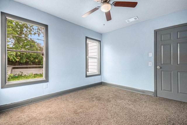 carpeted spare room featuring ceiling fan, visible vents, plenty of natural light, and baseboards
