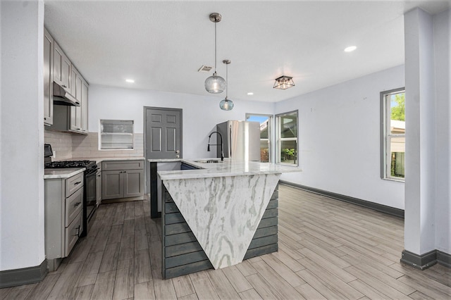 kitchen with black gas range oven, a sink, gray cabinets, under cabinet range hood, and visible vents