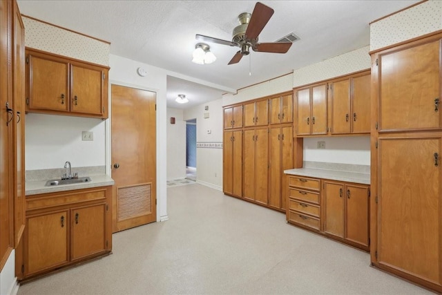 kitchen featuring brown cabinets, a sink, light countertops, a ceiling fan, and visible vents