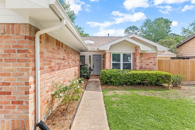 property entrance with a yard, a shingled roof, brick siding, and fence