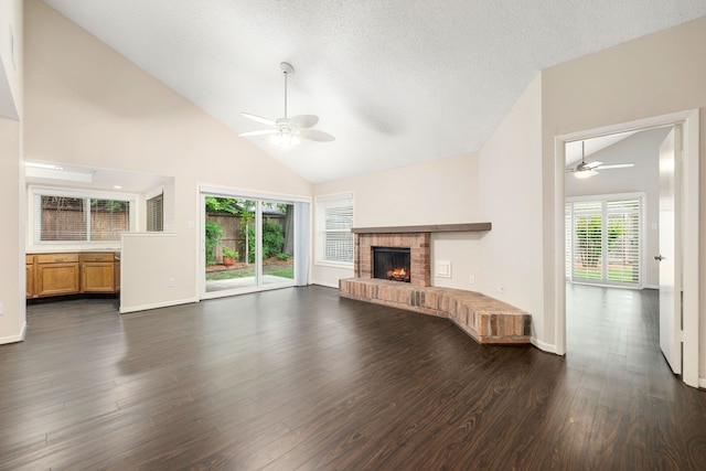 unfurnished living room featuring dark wood-style flooring, a brick fireplace, a ceiling fan, and a wealth of natural light