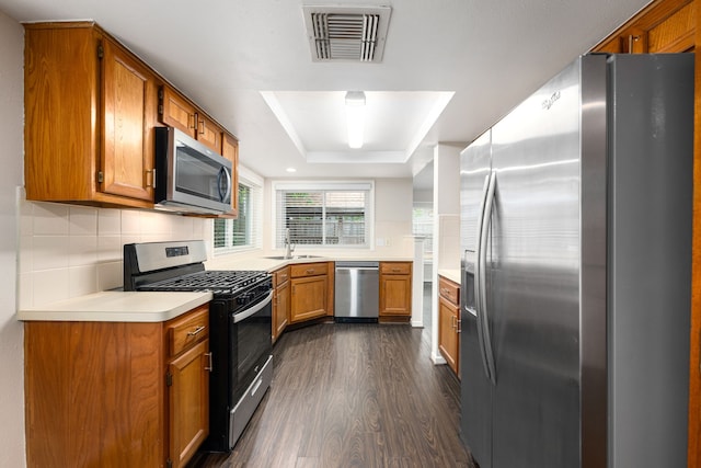 kitchen featuring brown cabinetry, dark wood-style flooring, visible vents, a raised ceiling, and stainless steel appliances