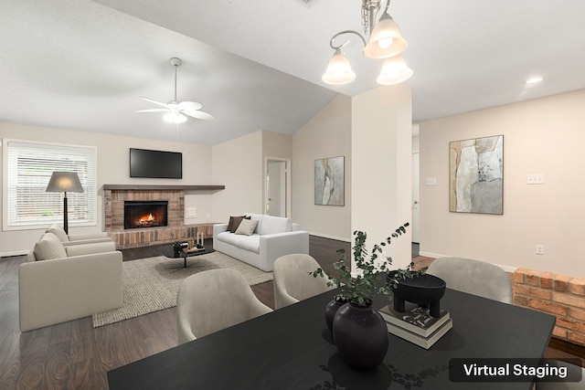 dining area with ceiling fan with notable chandelier, wood finished floors, vaulted ceiling, a brick fireplace, and baseboards