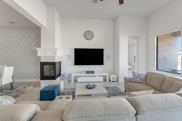 living area featuring light tile patterned floors, a tiled fireplace, baseboards, and a ceiling fan