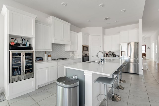 kitchen featuring stainless steel appliances, a sink, beverage cooler, backsplash, and a breakfast bar area