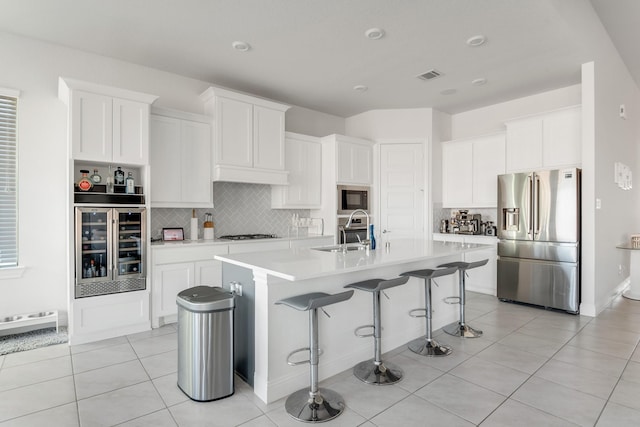 kitchen featuring stainless steel appliances, beverage cooler, a sink, backsplash, and a breakfast bar