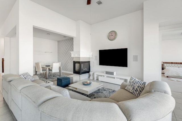 living area with light tile patterned floors, a tiled fireplace, and ceiling fan