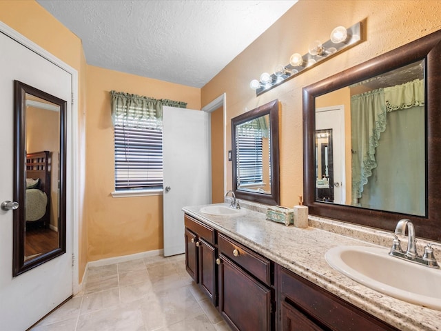 11602 Stone Bridge Dr, Houston, TX 77064 - bathroom featuring double vanity, a textured ceiling, baseboards, and tile patterned flooring