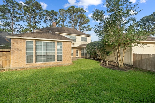rear view of property featuring a lawn, a chimney, a fenced backyard, and brick siding