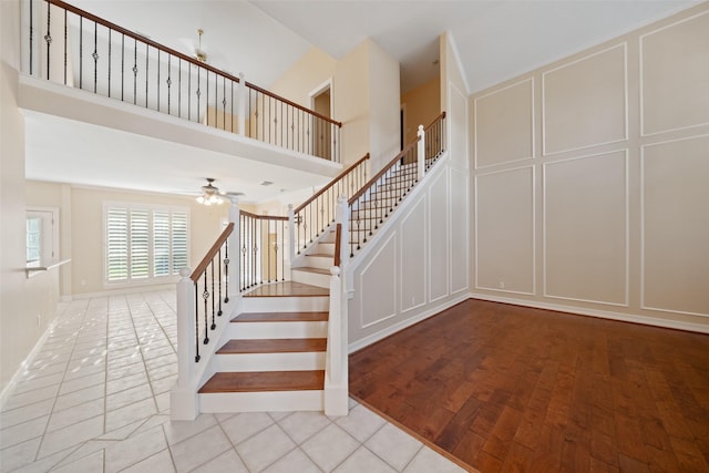 stairs featuring a ceiling fan, a towering ceiling, a decorative wall, and tile patterned floors