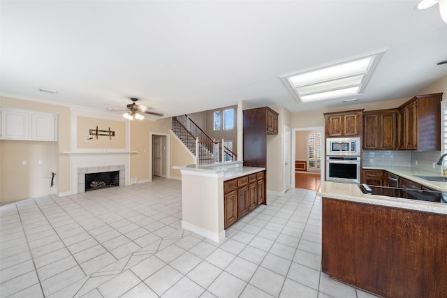 kitchen featuring appliances with stainless steel finishes, tasteful backsplash, a sink, a ceiling fan, and a tile fireplace