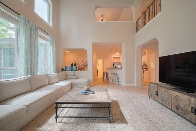 living area with light colored carpet, arched walkways, baseboards, a high ceiling, and light tile patterned flooring