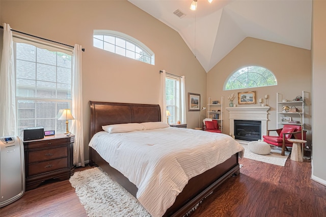 bedroom with visible vents, a glass covered fireplace, wood finished floors, and high vaulted ceiling