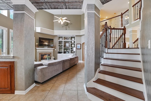 staircase with tile patterned flooring, a towering ceiling, a fireplace, built in shelves, and a ceiling fan
