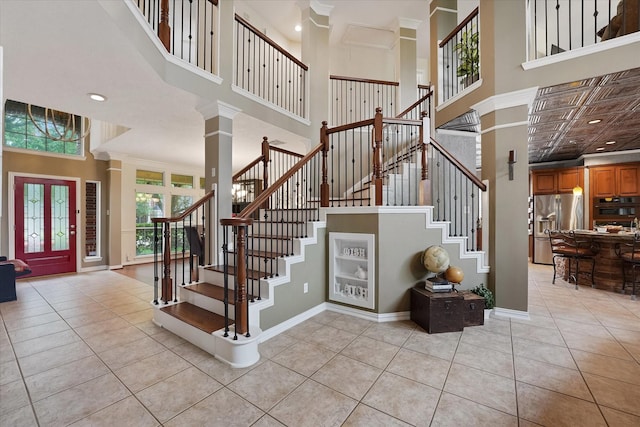 stairs featuring tile patterned flooring, recessed lighting, baseboards, decorative columns, and a towering ceiling